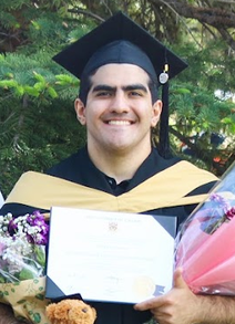 Mehdi in graduation attire holding his degree and flowers